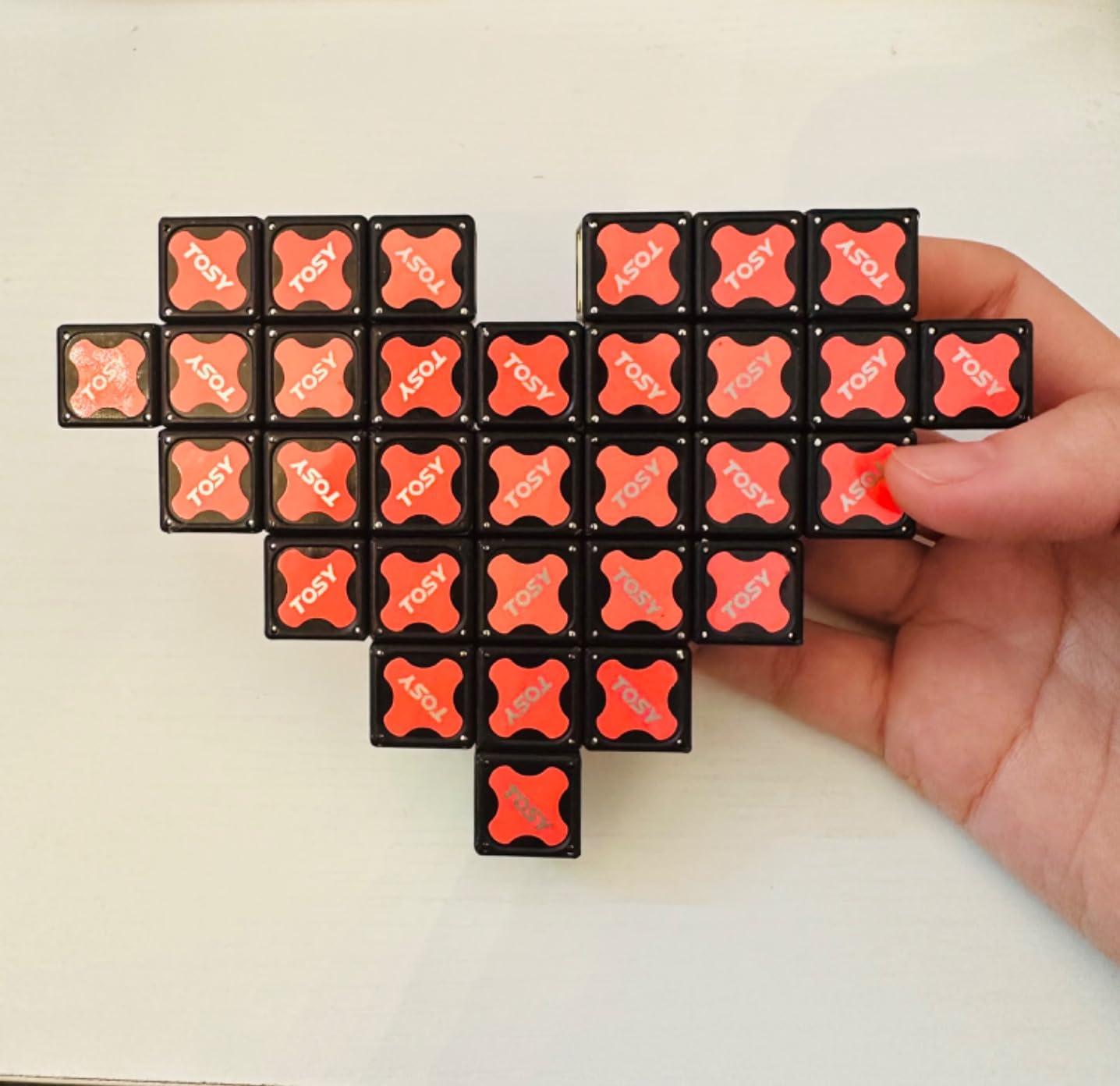 Hand holding a Rubik's-like puzzle with red and black pieces on a white background